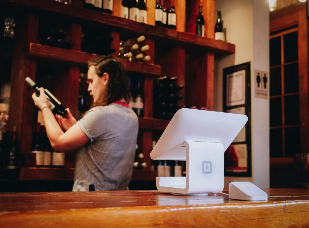 Employee checking a wine bottle behind the counter to sell. On the counter is a POS system.